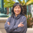 May Leong, an Asian American woman wearing a gray jacket against a brightly colored background
